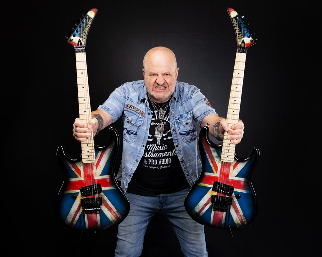 Nick Bowcott holding two guitars looking at the camera agressively